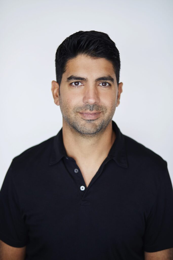A professional-looking man with short dark hair and a beard, wearing a black polo shirt, posed against a plain white background.